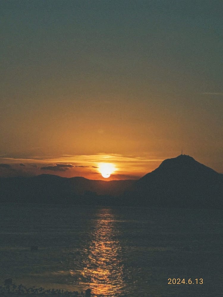 The sun setting behind a mountain over the water